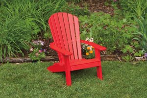 Bright red poly furniture Adirondack chair sitting in the grass outside.