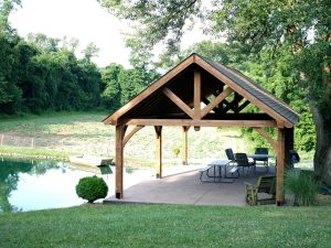 18x32 Open A-Frame Pavilion made with timberwood and asphalt roofing stands next to a pond with tables and chairs underneath it.