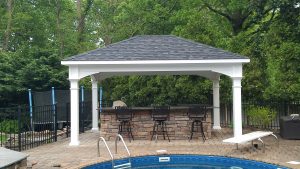 White vinyl Standard Pavilion with gray shingle roofing standing over a bar and grill with counter chairs in front of a pool.