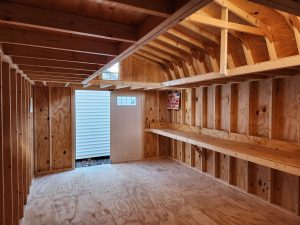 inside empty shed with shelves, a loft, an an open door