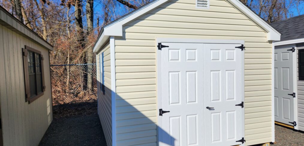 a-frame shed with white double doors, cream siding, and windows with blue shutters on the side